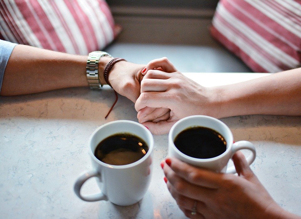 2人分のコーヒーと手を重ねる2人